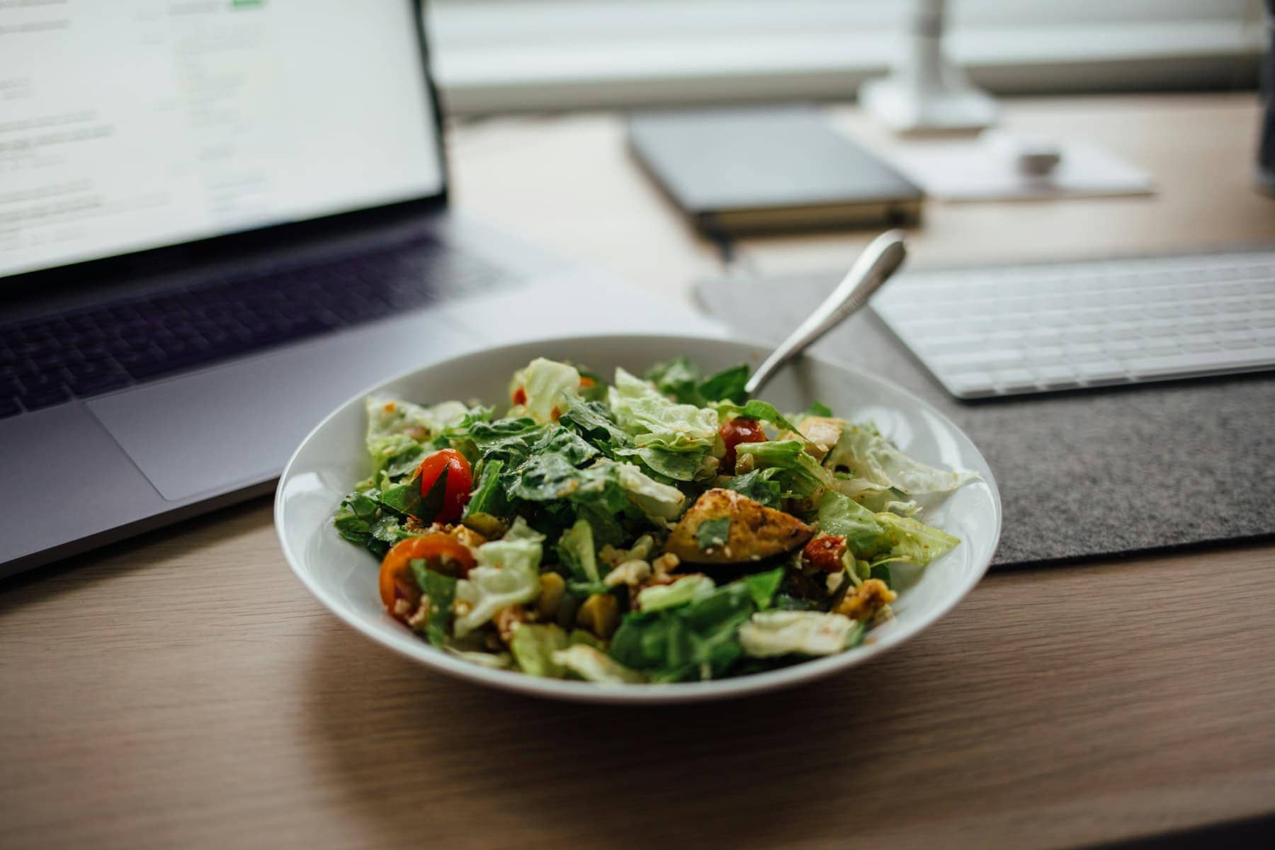 Un bol de salade posé sur un bureau, à côté d’un ordinateur portable