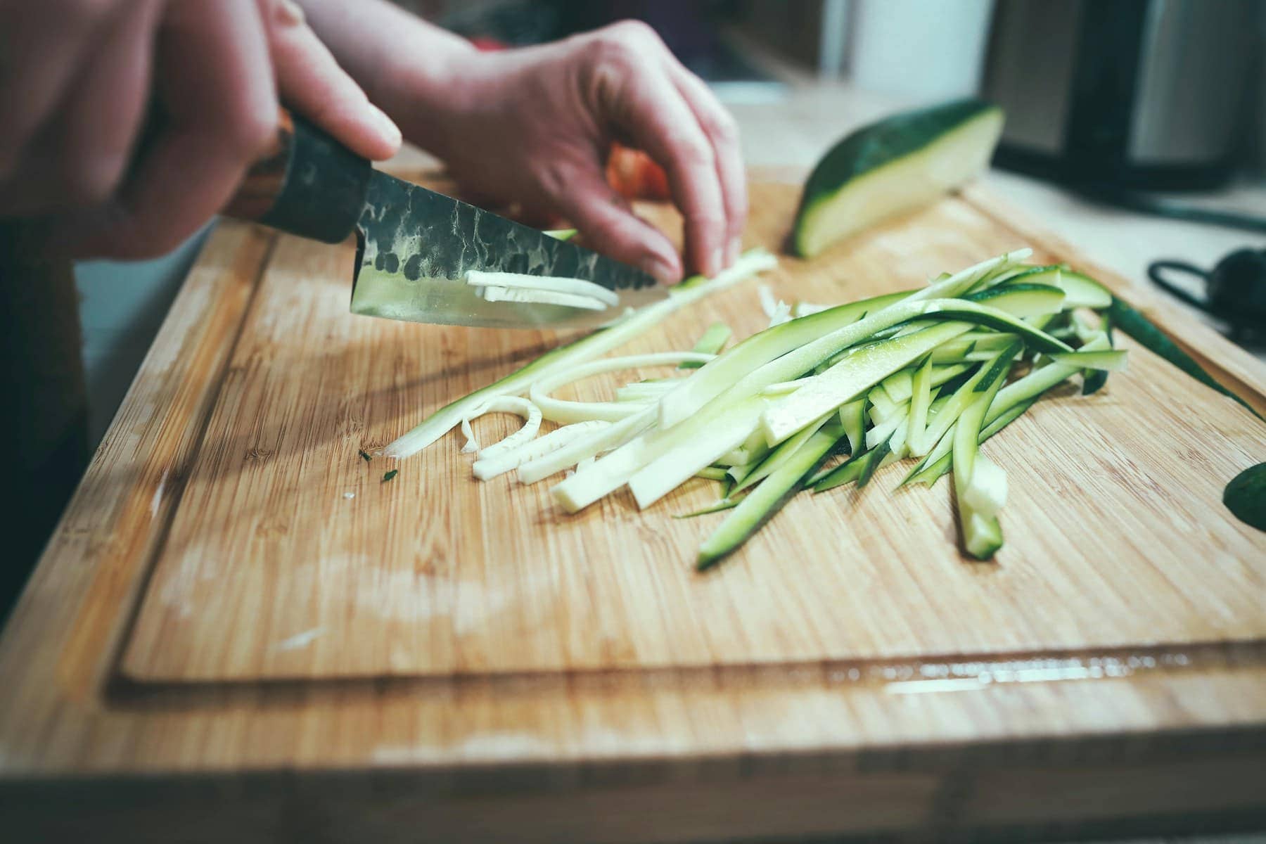 Des mains découpant un concombre sur une planche à découper